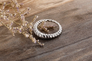 Macro detail of silver croissant ring with twisted texture on a natural wooden surface
