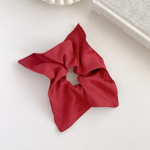 Flat lay of a red silk satin scrunchie next to a book on a clean white background