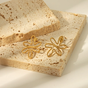Détail des boucles d'oreilles fleur dorée avec pétales ajourés sur socle en pierre beige