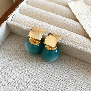Macro view of gold brushed square studs with dark green resin ball drop earrings