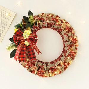 LED Christmas linen wreath with red berries, pine cones and a plaid bow on white surface