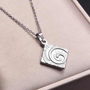 Macro view of a square silver pendant with spiral floral textures on a link chain