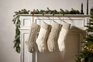 Detail view of four knit Christmas stockings with cable patterns on a white fireplace mantle