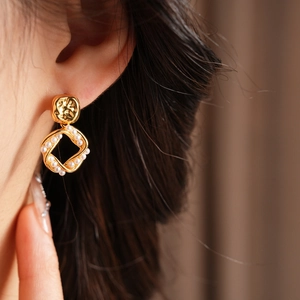 Close-up of gold-plated square hoop earrings with pearl accents worn by a model