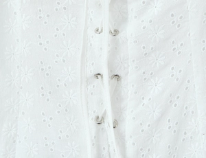 Detailed view of white broderie anglaise fabric with metal eyelets and lace-up design