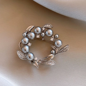 Detailed close-up of wreath brooch with grey pearls and sparkling crystals on silk background