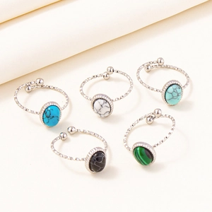 Detailed view of five adjustable silver rings with colorful marble stones on beige fabric