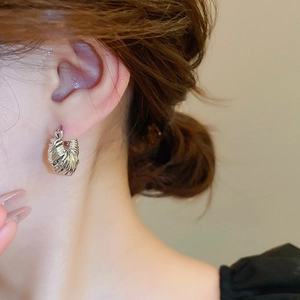 Close-up of a silver U-shaped earring with twisted texture on a model's ear