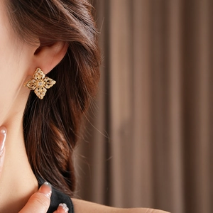 Detail of a hollow gold flower stud earring with zircon on a female model ear