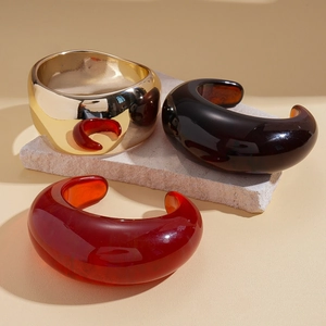 Retro resin and gold open cuff bracelets in amber and burgundy on stone pedestal