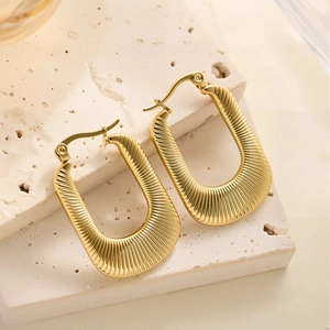 Détail macro de boucles d'oreilles en U dorées avec texture plissée et fermoir classique
