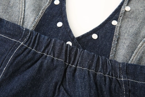Detail of dark blue denim halter top showing elastic pleated waist and white buttons