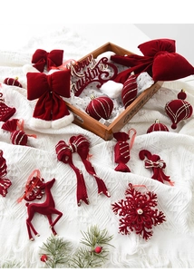 Detail of red velvet Christmas ornaments including bells, elk, and bows on wood tray