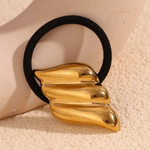 Macro detail of a gold wing-shaped hair tie on a minimalist beige texture background