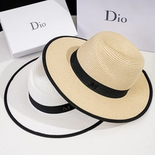 Detail view of woven straw hats in beige and white with black ribbon and metal M logo