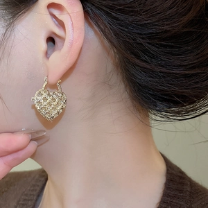 Close-up of heart-shaped hollow mesh earrings with gold plating and sparkling rhinestones