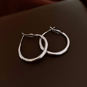 Detailed close-up of polished silver hoop earrings on a premium leather surface