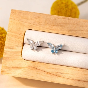 Elegant butterfly screw earrings in silver with clear and blue crystals on a wood box