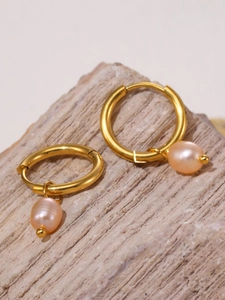Close-up of 18k gold-plated hoop earrings with baroque pearl pendants on a stone surface