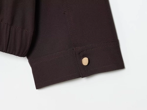 Détail macro du poignet de la veste marron avec bouton pression doré et bordure élastique