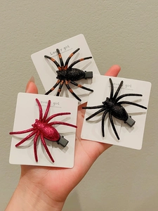 Detailed view of three glittery spider hair clips in black, red, and orange colors
