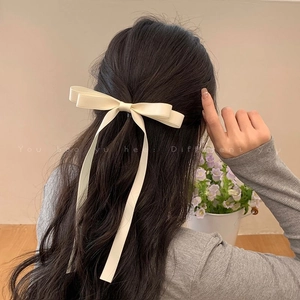 Detail of cream satin bow hair clip with long ribbons worn on a half-up hairstyle
