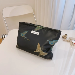 Detail of butterfly embroidery on black jacquard fabric cosmetic bag with brand label