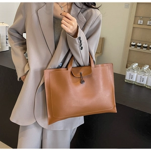 Detailed view of a brown vintage leather tote bag with button flap on a textured desk