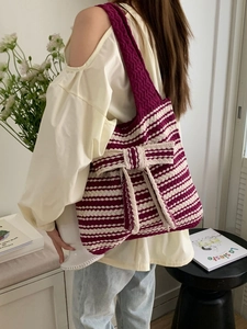 Detail of knitted tote bag with red stripes and oversized bow worn by a model