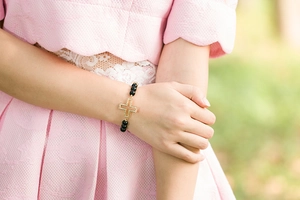 Close-up of black beaded bracelet with gold rhinestone cross charm worn by a model