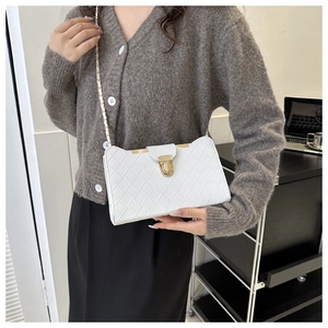 Detail of white woven crossbody bag featuring a gold clasp and metal chain strap
