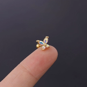 Macro view of a tiny gold butterfly earring with iridescent zircons on a fingertip