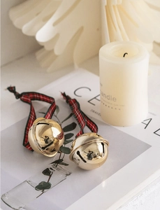 Detail of two golden Christmas bells with red and black plaid ribbons on a cozy background