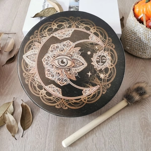 Detail of Shamanic drum with golden moon and sun symbols on black surface with drumstick