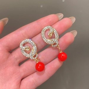 Close-up of gold snake earrings with sparkling crystals and a vibrant red bead detail