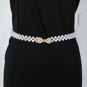 Close-up of elegant white pearl belt with a sparkling gold diamond bow buckle on dress
