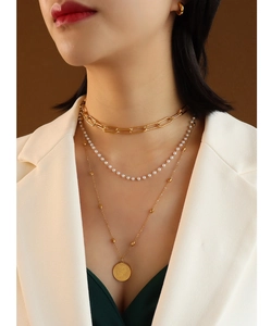 Detailed view of triple-layered gold chain necklace with pearl and coin pendant on model