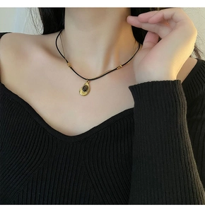 Close-up of a vintage double-layer necklace with a gold teardrop pendant on a black sweater