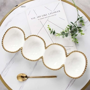 Close-up of four-grid ceramic appetizer platter with elegant gold beaded trim and spoon