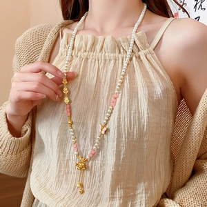 Detail of a long pearl necklace with golden butterfly pendant and silk tassel on model