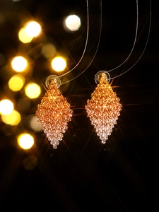 Macro detail of diamond-encrusted rhombus earrings with orange to silver gradient