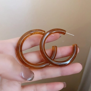 Handheld shot of amber resin C-shaped hoop earrings featuring a French retro design