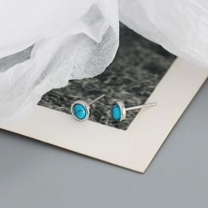 Macro shot of minimalist silver turquoise stud earrings on white textured background