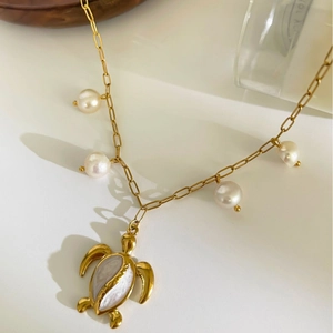 Elegant gold turtle necklace with freshwater pearls and mother of pearl inlay on white table