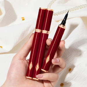 Macro shot of dark red liquid eyeliner with gold ring and fine brush tip on white fabric