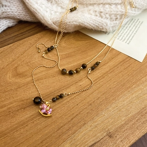 Détail d'un collier doré double épaisseur avec perle œil de tigre et pendentif cheval à bascule