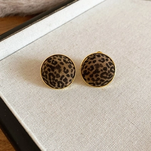 Detailed view of round leopard print earrings with gold frames on a display tray