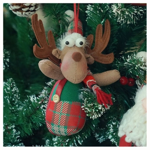 Close-up of Christmas reindeer ornament with plaid scarf hanging on a festive pine tree