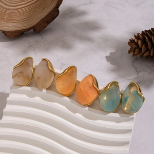 Three pairs of waterdrop resin earrings in gold setting on a wavy stand with marble decor