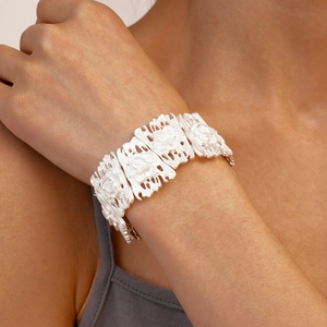 Detailed view of wide silver hollow floral bangle with matte geometric texture on wrist